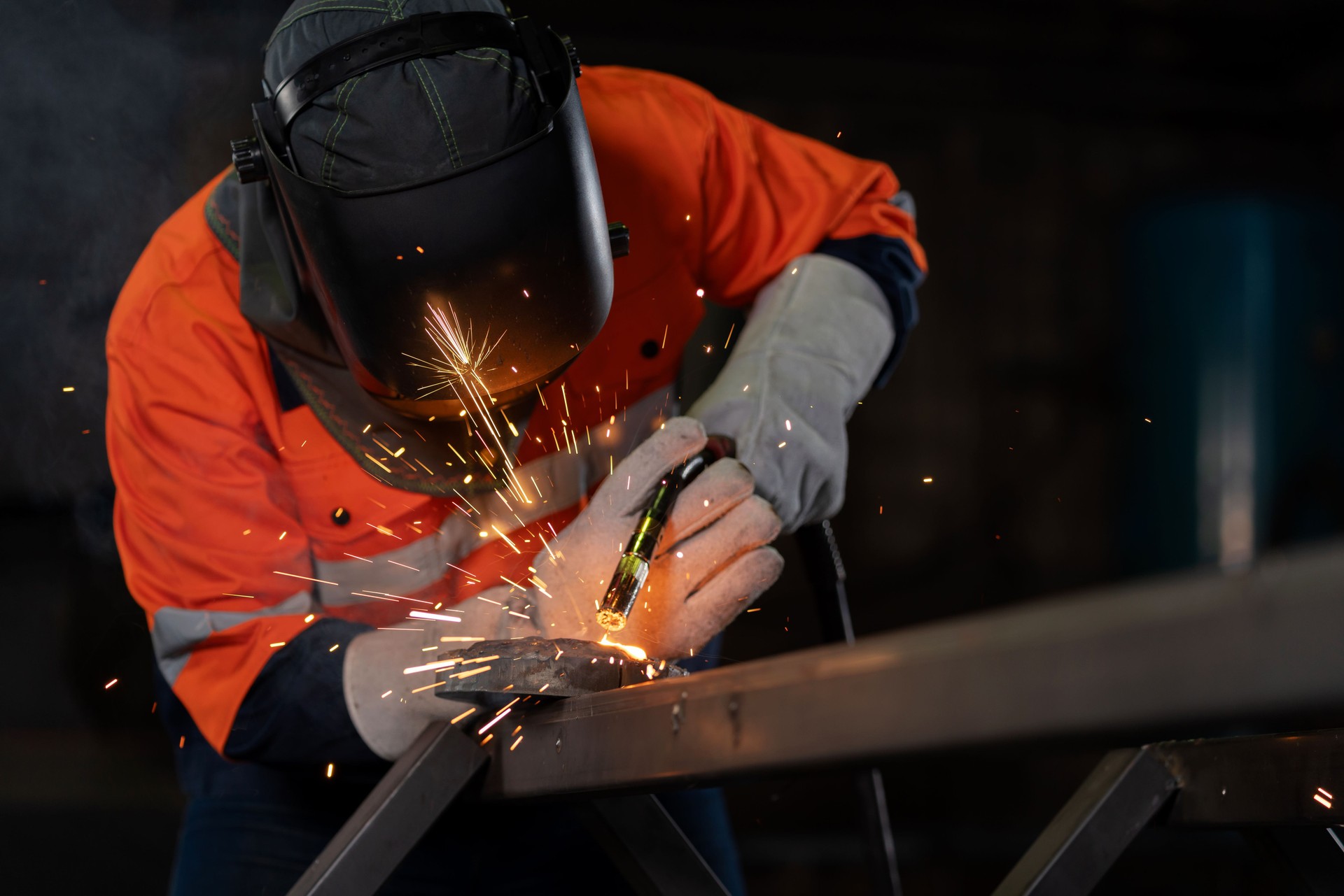 Engineer in protective suit expertly welds steel, creating a mesmerizing display of sparks that seem to dance and spread like a beautiful spectacle. Professional is contributing to the manufacturing process, adding value and strength to steel components.